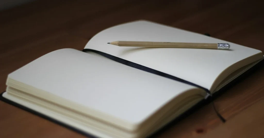 Person writing in an open journal at a kitchen table in soft morning window light
